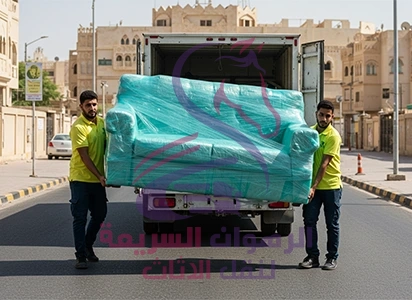 "فريق شركة نقل عفش بجدة ينقل كنبة مغلفة من الشاحنة إلى المنزل بعناية لضمان تسليم آمن وخالٍ من أي تلف "